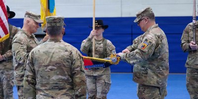 U.S. Army Col. Frank Tantillo, commander of the 86th Infantry Brigade Combat Team (Mountain), Vermont National Guard, and Command Sgt. Maj. Andrew Campagne, command sergeant major of the 86th Infantry Brigade Combat Team (Mountain), unfurl the brigade colors during a Joint Multinational Training Group–Ukraine transfer of authority ceremony at Grafenwoehr Training Area, Germany, Feb. 18, 2026.