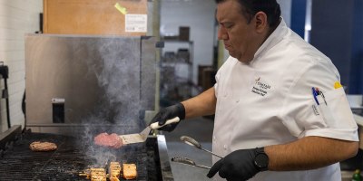 Enrique Estrada, executive chef for 42 Bistro, Compass Group USA, Inc., tends to burgers and salmon on a grill Feb. 12 at 42 Bistro at Fort Hood. Estrada oversees back-of-house operations, managing kitchen staff and ensuring recipes, portion control and food quality meet Compass standards. (U.S. Army photo by Pfc. Patrick M. Connery)