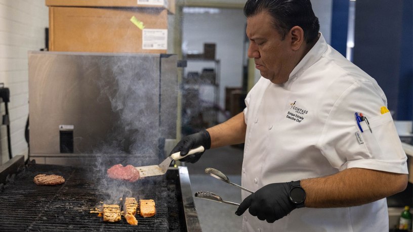 Enrique Estrada, executive chef for 42 Bistro, Compass Group USA, Inc., tends to burgers and salmon on a grill Feb. 12 at 42 Bistro at Fort Hood. Estrada oversees back-of-house operations, managing kitchen staff and ensuring recipes, portion control and food quality meet Compass standards. (U.S. Army photo by Pfc. Patrick M. Connery)