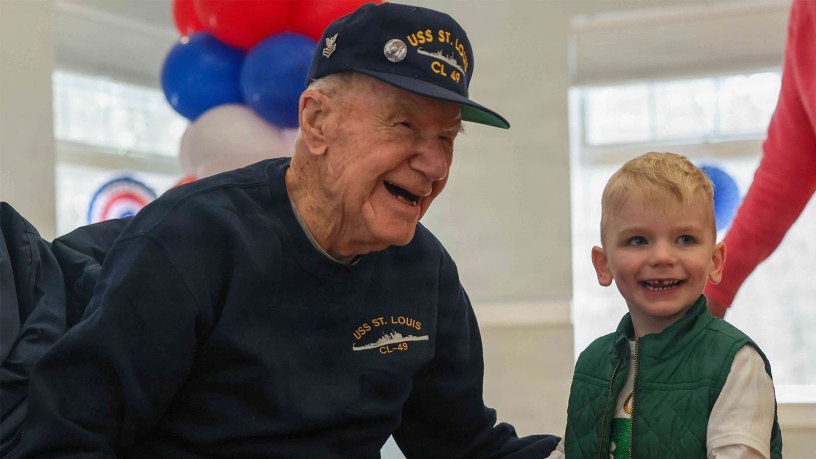 Freeman Johnson greets his great-grandson, Owen McGrath, during his 106th birthday party at the Barnstable Adult Community Center in Hyannis, Mass., March 18, 2026. Johnson, one of the oldest survivors of the attack on Pearl Harbor, Hawaii, was stationed aboard the USS St. Louis on the morning of the attack.