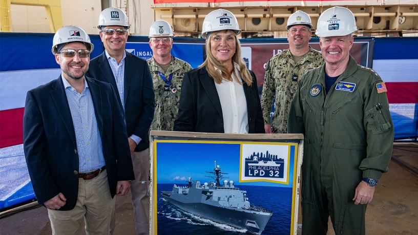 Mrs. Maureen Paparo, sponsor for LPD 32, Philadelphia, and other platform guests pose for a group photo behind the weld stand at Ingalls Shipbuilding in Pascagoula, Miss. March 3, 2026.