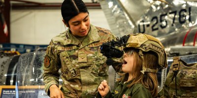 U.S. Air National Guard Airman 1st Class Glini Retana, a security forces specialist with the 103d Security Forces Squadron, helps a child try on a specialized headset at a Women Take Flight event on March 14, 2025, Windsor Locks, Connecticut. Multiple volunteers from the 103d supported this event with hands-on activities and speaking opportunities.