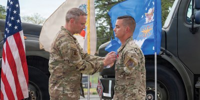 From right, U.S. Air Force Master Sgt. Charles Zingrone, 177th Fighter Wing Logistics Readiness Squadron Petroleum, Oils and Lubricants (POL) fuels management flight chief, receives a Bronze Star medal from Col. Matthew Vanderschuere, 177th Fighter Wing Mission Support Group commander, during a presentation ceremony for Zingrone at the 177th POL facility, Egg Harbor Township, New Jersey, April 17, 2026. (U.S. Air National Guard photo by Senior Airman Connor Taggart)