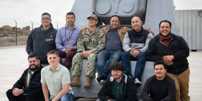 Directed energy team members with Naval Surface Warfare Center, Port Hueneme Division gather around the Optical Dazzling Interdictor, Navy (ODIN) behind the Directed Energy Systems Integration Laboratory (DESIL) onboard Naval Base Ventura County Point Mugu in California on Jan. 30, 2025. DESIL now offers courses on operating and maintaining ODIN, giving sailors and other students hands-on experience with the directed energy system in a training environment. (U.S. Navy photo by Eric Parsons)