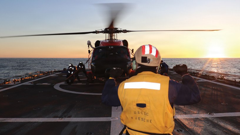 U.S. Coast Guard Ensign Garth Bowman, a landing signal officer assigned to U.S. Coast Guard Cutter Waesche (WMSL 751), directs an MH-60 Jayhawk helicopter from Air Station Kodiak during flight operations in the Bering Sea, Feb. 21, 2026. Training is essential to maintaining unit readiness and proficiency for Waesche and the air stations. (U.S. Coast Guard photo by Petty Officer 3rd Class Christian Swenk)