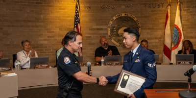 Fort Walton Beach Police Department Chief Robert Bage, left, presents Senior Airman Marcus Wu, right, assigned to the 1st Special Operations Wing, with a certificate of appreciation during a city council meeting in Fort Walton Beach, Florida, May 19, 2026. Wu was recognized for his heroic actions during an off-duty emergency response in which he helped save a woman during a dog attack. (U.S. Air Force photo by Airman 1st Class Alexa Hunt)