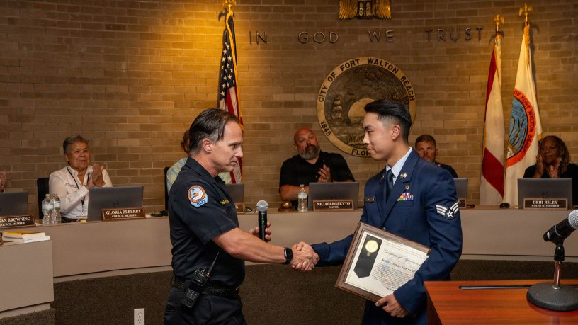 Fort Walton Beach Police Department Chief Robert Bage, left, presents Senior Airman Marcus Wu, right, assigned to the 1st Special Operations Wing, with a certificate of appreciation during a city council meeting in Fort Walton Beach, Florida, May 19, 2026. Wu was recognized for his heroic actions during an off-duty emergency response in which he helped save a woman during a dog attack. (U.S. Air Force photo by Airman 1st Class Alexa Hunt)