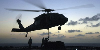 A Navy MH-60S Seahawk helicopter hovers over the flight deck of the USS Bataan (LHD 5) as crewmembers hook up cargo during a vertical replenishment as the ship operates in the Caribbean Sea on May 27, 2006.