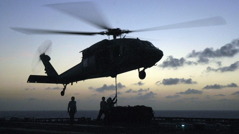A Navy MH-60S Seahawk helicopter hovers over the flight deck of the USS Bataan (LHD 5) as crewmembers hook up cargo during a vertical replenishment as the ship operates in the Caribbean Sea on May 27, 2006.