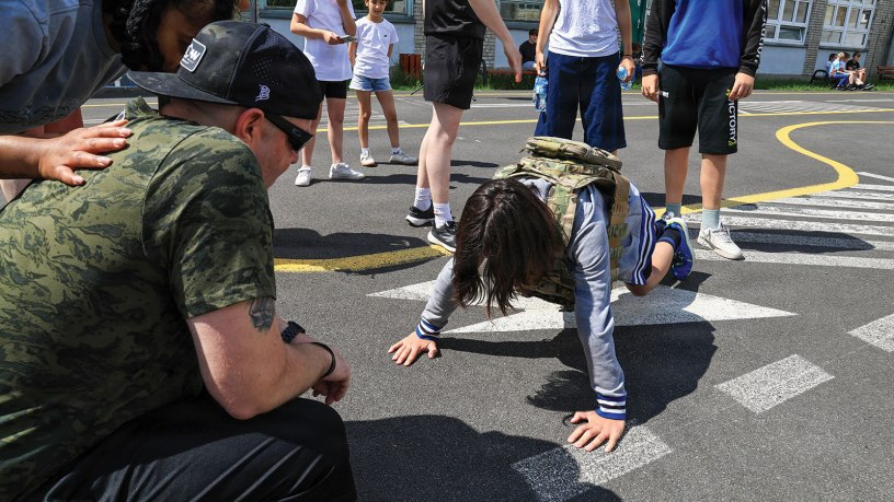 U.S. Army Reserve Staff Sgt. Joseph Callaway, signal support sergeant with the 418th Civil Affairs Battalion, 308th Civil Affairs Brigade, 353rd Civil Affairs Command, watches as the child is doing pushups with military apparel from the Primary school on June 01, 2026, in Poznan, Poland.