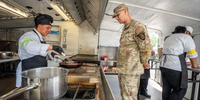 Sgt. Malik Durden, righ, a 92G Culinary Specialist with the Oregon Army National Guard, talks with Kyan Lor, left, chef for one of the entree teams at the Career Technical Education Center, as Lor cooks a Mongolian beef dish in a fry pan inside an Army Containerized Kitchen during the "Chopped Challenge" competition in Salem, Oregon, June 4, 2026.