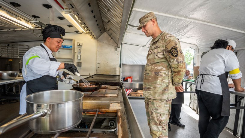 Sgt. Malik Durden, righ, a 92G Culinary Specialist with the Oregon Army National Guard, talks with Kyan Lor, left, chef for one of the entree teams at the Career Technical Education Center, as Lor cooks a Mongolian beef dish in a fry pan inside an Army Containerized Kitchen during the "Chopped Challenge" competition in Salem, Oregon, June 4, 2026.