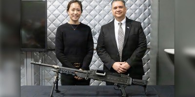 M240 Armaments Project Officer Rose Tai and Welding and Non-Destructive Testing technician for Methodologies Laboratories at Quality Engineering & System Assurance Henry Sanchez stand behind a model of the M240 machine gun, complete with an improved bipod with a single component Lower Leg.