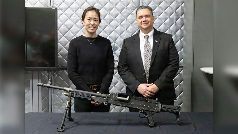 M240 Armaments Project Officer Rose Tai and Welding and Non-Destructive Testing technician for Methodologies Laboratories at Quality Engineering & System Assurance Henry Sanchez stand behind a model of the M240 machine gun, complete with an improved bipod with a single component Lower Leg.