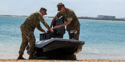 U.S. Marine Corps. Lt. Col. Michael Radigan and Lt. Evan Humphrey, a student at the Naval Postgraduate School, load cargo onto a digitally crewed surface vessel at the Honolulu Harbor Public Boat Ramp during Exercise Rim of the Pacific 2026 in Honolulu, Hawaii, July 7, 2026.