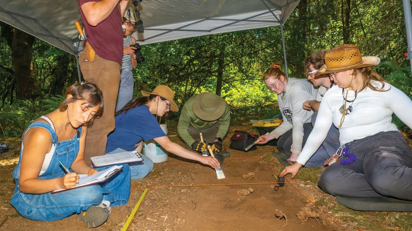 Oregon State University Archaeology Field School students document a test unit as Andrew Pauly, standing, a graduate teaching assistant, photographs the excavation at Najaf Training Center, Ore., July 14, 2026.