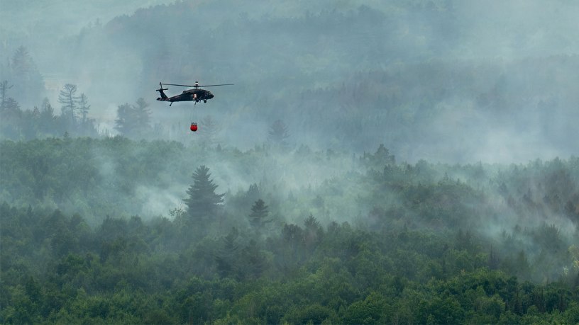 A U.S. Army National Guard UH-60 Black Hawk helicopter assigned to the 34th Combat Aviation Brigade transports water in a Bambi Bucket over wildfires in Northern Minnesota, July 15, 2026.