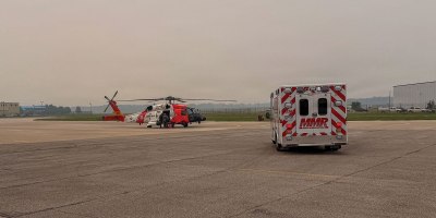 A U.S. Coast Guard Air Station Traverse City MH-60 Jayhawk helicopter and a local emergency medical services ambulance sit on the tarmac at the air station in Traverse City, Michigan, July 17, 2026.