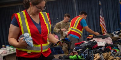 A volunteer for an Emergency Family Assistance Center folds donated clothes on Fairchild Air Force Base, Washington, August 2, 2026. The Fairchild Military Family and Readiness Center activated the EFAC to provide support to military families who were impacted by wildfires across the region through donations and assistance resources. (U.S. Air Force photo by Staff Sgt. Emily Farnsworth)