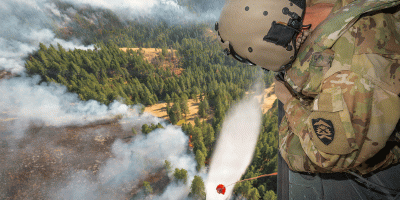 U.S. Army Staff Sgt. Kyle Sanders, a crew chief with Golf Company, 1st Battalion, 189th Aviation, watches as water releases from an HH-60M Black Hawk helicopter's bucket onto the Hagen Fire in Umatilla County, Ore., Aug. 10, 2026.