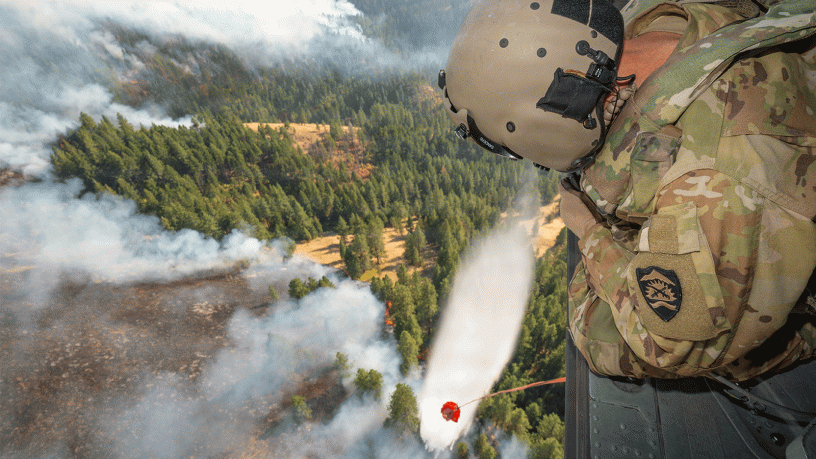 U.S. Army Staff Sgt. Kyle Sanders, a crew chief with Golf Company, 1st Battalion, 189th Aviation, watches as water releases from an HH-60M Black Hawk helicopter's bucket onto the Hagen Fire in Umatilla County, Ore., Aug. 10, 2026.