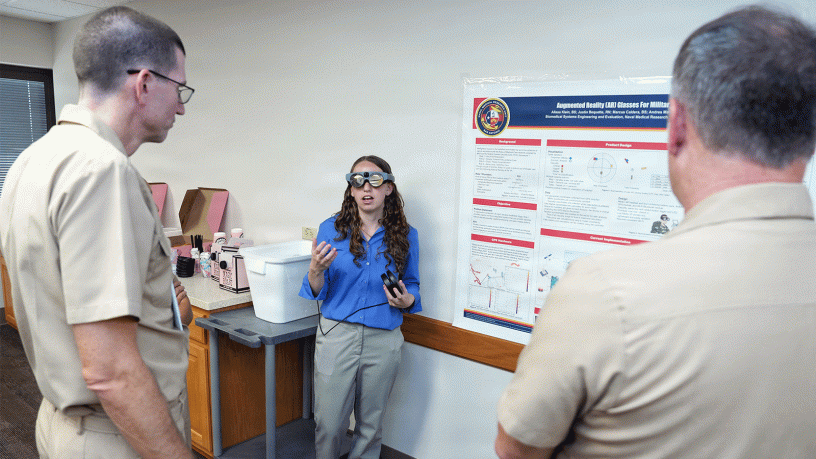 Alissa Klein, of Agoura Hills, Calif., an intern assigned to Naval Medical Research Unit (NAMRU) San Antonio, presented research on augmented reality glasses for military medics to Cmdr. Nicholas Hamlin, executive officer and Lt. Cmdr. Cameron Burnett, director, Directed Energy Health Affects, at the Battlefield Health and Trauma Research Institute.