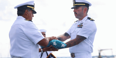 Lt. j.g. Robbie Baca, medical administrative officer and flag detail assigned to the Wasp-class amphibious assault ship USS Bataan (LHD 5), passes a historic handmade flag to Capt. Rodolfo Jacobo, the commanding officer of Bataan, during a ceremony commemorating the 81st anniversary of Victory Over Japan Day on the ship's flight deck, Aug. 15, 2026.