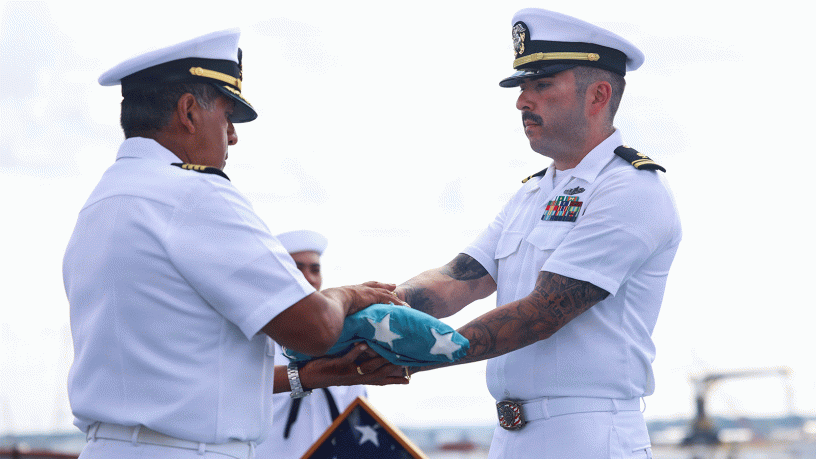 Lt. j.g. Robbie Baca, medical administrative officer and flag detail assigned to the Wasp-class amphibious assault ship USS Bataan (LHD 5), passes a historic handmade flag to Capt. Rodolfo Jacobo, the commanding officer of Bataan, during a ceremony commemorating the 81st anniversary of Victory Over Japan Day on the ship's flight deck, Aug. 15, 2026.