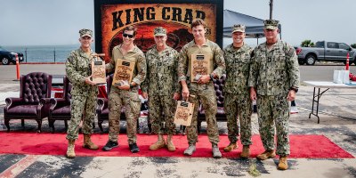 The official party poses for a photo with the winners from Explosive Ordnance Disposal Mobile Unit 2, Explosive Ordnance Disposal Technician 1st Class Nick Wiencek and Explosive Ordnance Disposal Technician 3rd Class James Vosler at the King Crab 2026 awards ceremony on Naval Amphibious Base Coronado, California, August 28, 2026.