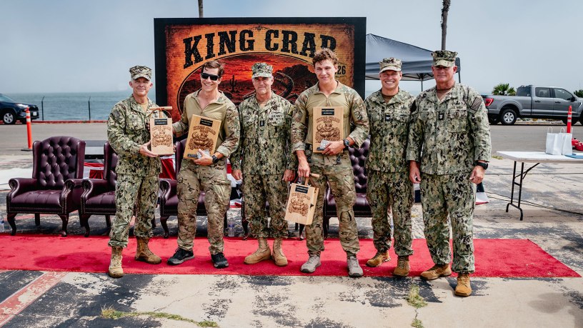 The official party poses for a photo with the winners from Explosive Ordnance Disposal Mobile Unit 2, Explosive Ordnance Disposal Technician 1st Class Nick Wiencek and Explosive Ordnance Disposal Technician 3rd Class James Vosler at the King Crab 2026 awards ceremony on Naval Amphibious Base Coronado, California, August 28, 2026.
