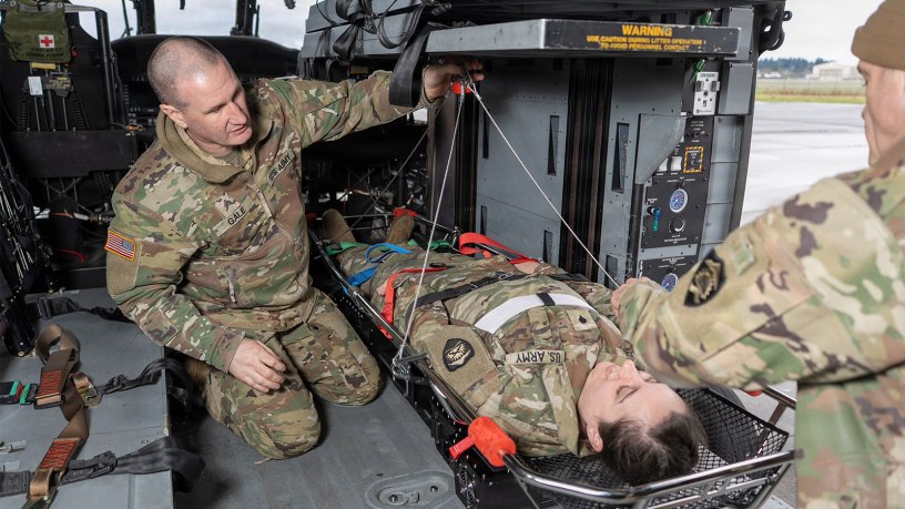 Sgt. James Gale, left, and Chief Warrant Officer 4 Josiah Zeiner, right, both with Golf Company, 1st Battalion, 189th Aviation Regiment, Oregon Army National Guard, practice securing the Vita hoist device to an HH-60M Black Hawk with a simulated patient, Spc. Stephanie Rider, at McNary Field Army National Guard Heliport in Salem, Oregon, Dec. 5, 2025. (U.S. Army National Guard photo by Maj. W. Chris Clyne, Oregon National Guard Public Affairs)