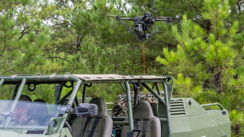 A tethered unmanned aerial system (Te-UAS) hovers behind an Infantry Squad Vehicle-Utility (ISV-U) during a Maneuver Battle Lab (MBL) assessment at McKenna Field Landing Site on Fort Benning, Ga., Aug. 6, 2026.