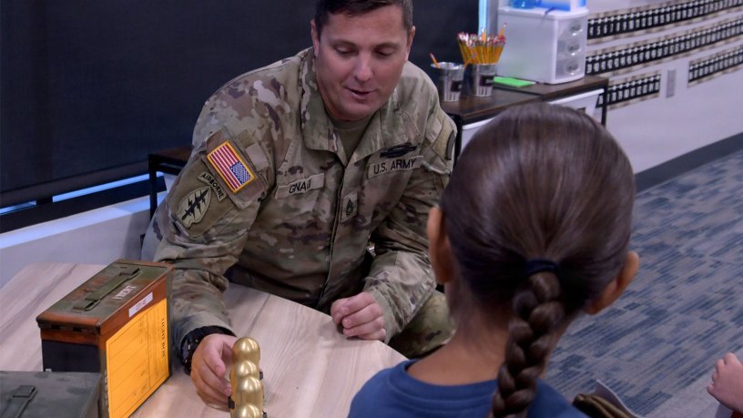 Sgt. 1st Class Will Gnagi shows a Townsend Elementary School first‑grade student inert training rounds during a safety presentation on identifying unexploded ordnance that may be encountered near the Limestone Hills Training Area. U.S. National Guard photo by Master Sgt. Michael Touchette.